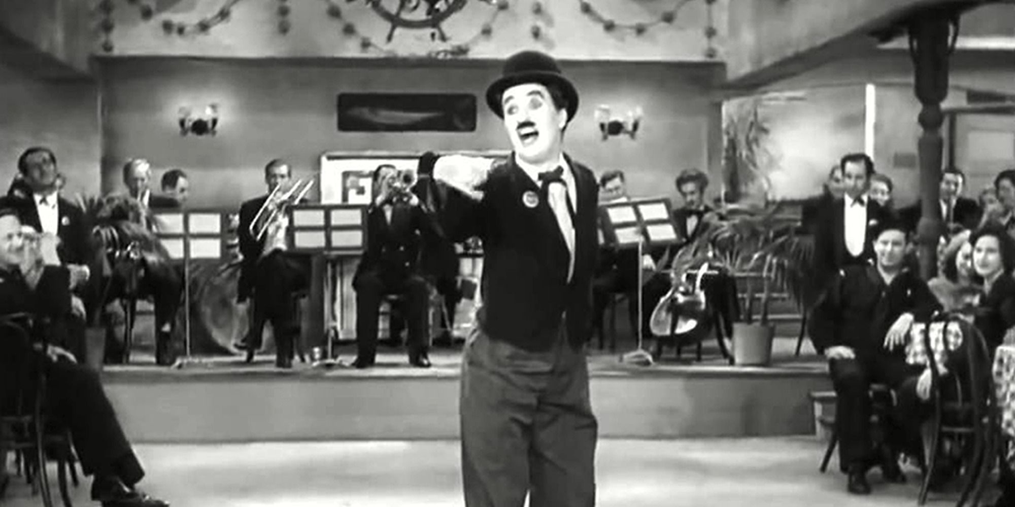 The Tramp singing a song in Modern Times with a band playing behind him and a crowd watching